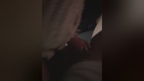 A dimly-lit, close-up video captures a dark-skinned person's hand holding a black object, possibly a gun, over a light-skinned person's chest. The setting is intimate and possibly tense, with blurred backgrounds.