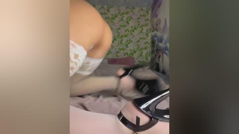 A blurry video of a woman in a white lace bra, black high heels, and a black mask, lying on a bed with floral wallpaper, in a dimly lit room.