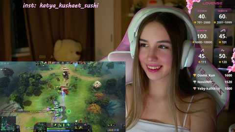 Media: Video of a smiling woman with light skin, long brown hair, wearing headphones, sitting in a gaming chair. Overlay of a League of Legends game scene.
