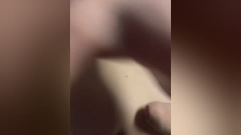 The image is a blurry video featuring a person, possibly male, with a light complexion, sitting or lying down on a bed. The background is dark, and the focus is unclear.