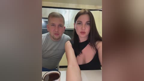 Media: Video of a Caucasian couple in a modern kitchen, man with short hair and a grey shirt, woman with long brown hair and black top, both holding coffee cups.