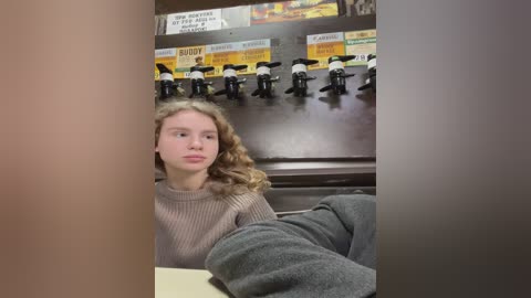 Media: Video of a young girl with curly blonde hair, wearing a beige sweater, seated at a table in a dimly lit restaurant with a row of toy horses above.