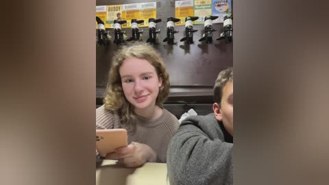 Media: Video of a young woman with curly blonde hair, wearing a beige sweater, sitting at a table in a fast-food restaurant. Behind her, beer taps and colorful signs are visible.