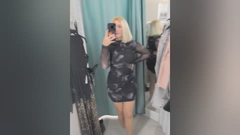 Video of a woman with straight, platinum blonde hair, wearing a sheer black mini dress with a leopard print pattern, standing in a brightly lit dressing room with teal curtains and hanging clothes.