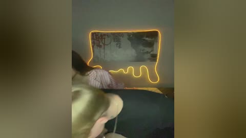 A video of a dimly lit room with a person in a striped shirt, facing a wall-mounted TV displaying a Japanese painting, illuminated by a glowing yellow light.