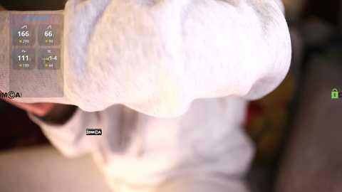 Media: A video of a person with a large, fluffy white towel covering their head, standing against a blurred background with a digital display showing temperature readings and \"Steam\" text.