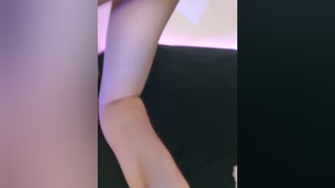 Media: A close-up video of a woman's right leg and torso, with smooth, pale skin and a black fabric sleeve. The background is blurred, featuring a mix of soft purple and white hues.