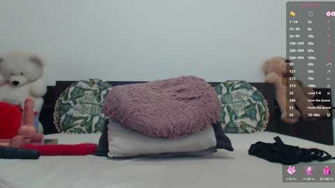 Video of a bed with a white sheet, a pink fluffy blanket, a teddy bear, a pillow with green leaves, and a black bra, overlaid with a digital sex game interface.