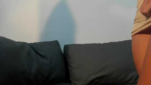 A video of a person wearing tan shorts, sitting on a black sofa against a blurred, light gray background.