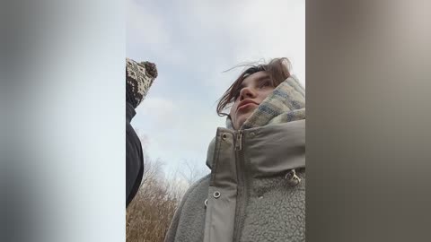 Media: A video captures a young man with tousled hair and a beige jacket, gazing upward at a bird perched on a wire. The background features a cloudy sky and bare trees.