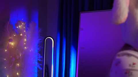Media: Video of a dimly lit room with a dark blue curtain, a glowing TV screen, and a decorative string of warm yellow fairy lights, creating a cozy, intimate ambiance.