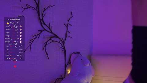 Video of a room bathed in purple light, featuring a white bear toy and a wall-mounted branch design with a digital clock and icons.