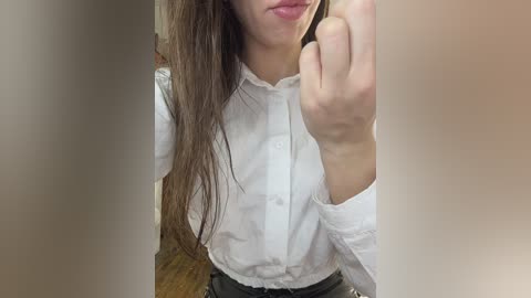 Media: A video of a young woman with long brown hair, fair skin, and a white blouse, giving a middle finger with her right hand, partially obscured by a blurred wooden wall.