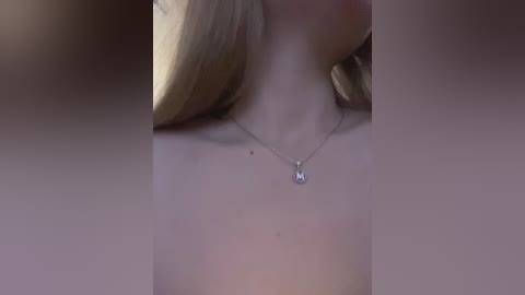 Video of a close-up view of a woman's neck and shoulders, wearing a delicate silver necklace with a small diamond pendant. Her long, straight blonde hair is partially visible. Background is blurred.
