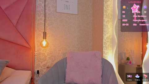 Video of a modern, cozy living room with a pink and beige color scheme. A light pink armchair with a fluffy pink throw pillow, a hanging Edison bulb lamp, and a decorative wall clock are visible.