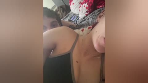 Media: A video shows a young woman with medium brown skin and dark hair, lying on a bed. She is wearing a black tank top and has a pierced navel. The bed has red and white patterned sheets.