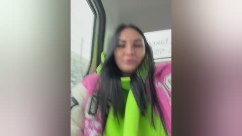 Video of a woman with long black hair, wearing a bright pink and green jacket, blurred face, inside a bus, with a window view of a snow-covered landscape.