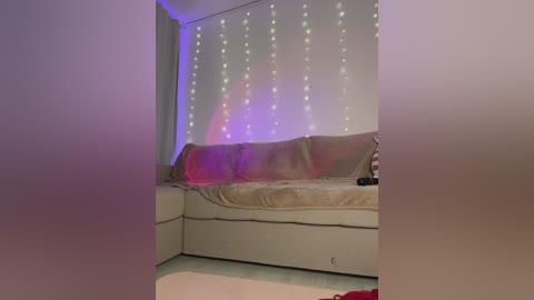 Video of a cozy, dimly lit living room with a beige sectional sofa, draped in sheer curtains adorned with fairy lights, and a red blanket partially covering it.