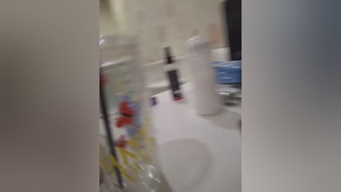Media: Video of a messy bathroom counter with multiple items, including a white toothbrush, a blue toothpaste tube, and a plastic bag. The background features a beige tiled wall. The image is slightly blurred.