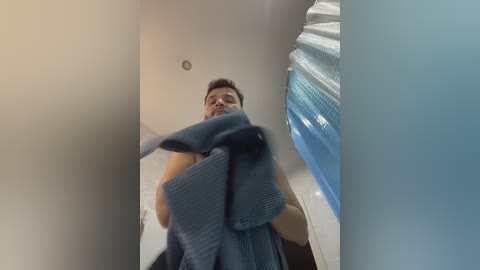 Media: Video of a man in a blue bathrobe, standing in a narrow hallway with a white ceiling and blue window on the right.