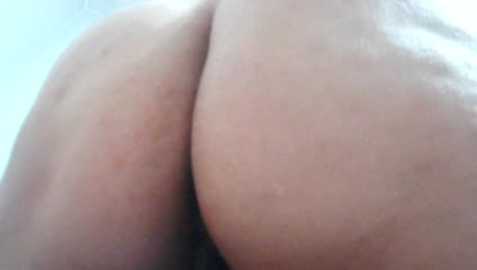 A close-up video of two light-skinned buttocks pressed together, showing smooth skin and a slight reddish hue. The background is out of focus, with a soft, blurred light source.