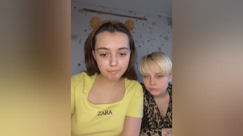 Media: Video of two young girls, one in a yellow Zara shirt, the other in leopard print, indoors with patterned wallpaper in the background.