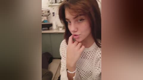 Media: Video of a young woman with long brown hair, wearing a white crochet top, posing seductively in a dimly lit bathroom with white tiles and a shelf holding toiletries.