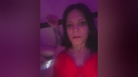 Video of a young woman with long dark hair, wearing a red bra, standing in a dimly lit room with purple lighting.