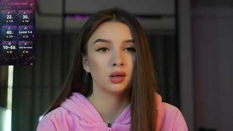 Media: Video of a young Caucasian woman with straight, long brown hair, wearing a pink hoodie, standing indoors with a blurred background. Left inset shows weather app.