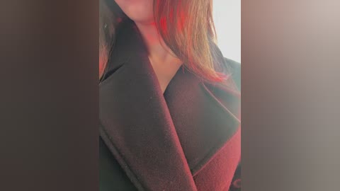 Media: A close-up video of a person's neck and shoulders, wearing a dark, textured jacket. The background is blurred with a warm, red hue, suggesting an intimate, possibly artistic setting.