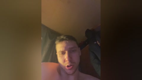 Media: A blurry video of a topless man with short dark hair, looking shocked, in a dimly lit room with a ceiling fan.