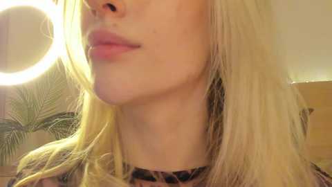 Media: A close-up video of a fair-skinned woman with straight blonde hair, wearing a leopard print top. Background shows a circular ring light and a green leafy patterned wall.