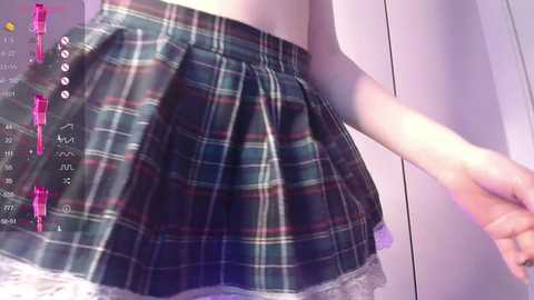 Media: Video of a young woman with pale skin, wearing a plaid mini skirt with a lace hem, standing in a room with a purple wall and white furniture.