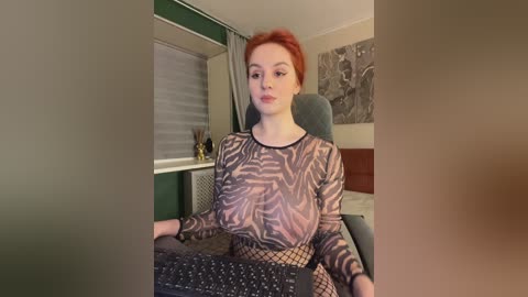 Media: Video of a pale-skinned woman with red hair, wearing a sheer, zebra-patterned top and fishnet tights, sitting in a green chair in a dimly lit room.