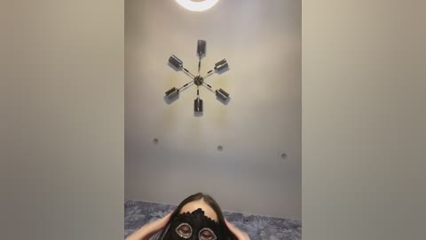 Media: A video of a ceiling with a modern, circular chandelier and a person's head in a black mask, viewed from below.