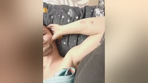 Video of a fair-skinned man with a beard, lying on a bed with a gray and white patterned sheet, holding a teal water bottle.