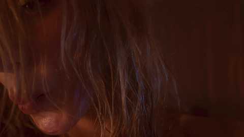 Media: Close-up video of a woman with wet, dark brown hair, eyes partially closed, looking sad or contemplative. The background is dark and blurred, emphasizing her face.