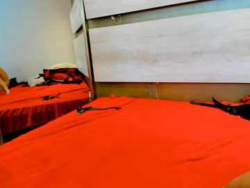 Media: A video of a simple, sparsely furnished room with two beds covered in vibrant red blankets, a beige wall, and a white wooden headboard.