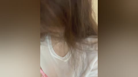 Media: Video of a woman with long brown hair, wearing a white tank top, partially visible. The background is blurred, focusing on the upper torso.