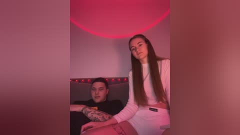 Media: Video of a tattooed man in a black shirt, sitting next to a slender, long-haired woman in white, in a dimly lit room with a red light.