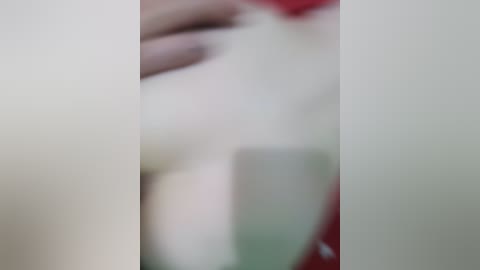 Blurred video of a person with light skin, wearing red clothing, with a hand on their chest.
