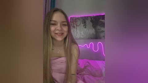Video of a young, smiling Caucasian woman with long, blonde dreadlocks in a pink strapless dress. Neon pink lights illuminate the background with graffiti and a bed in a dimly lit room.
