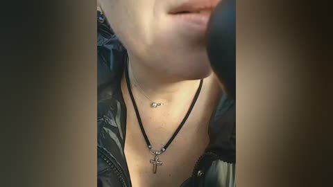 A close-up video of a woman with fair skin, wearing a black leather jacket, a black necklace with a crucifix pendant, and a silver ring, with blurred background.