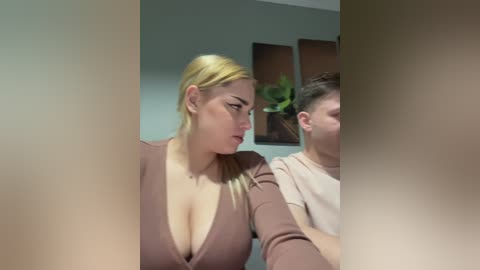 A video of a blonde woman in a low-cut brown top and a young man in a beige shirt, both looking towards the camera, with blurred edges.