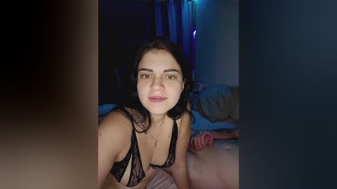 Video of a young woman with olive skin, dark hair, and dark eyes, wearing black lace lingerie, lying on a bed with a blurred background.