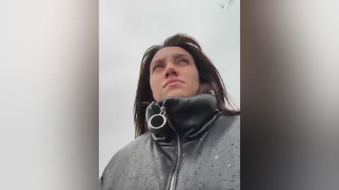 Media: Video of a young woman with long dark hair, wearing a black leather jacket with a metal ring on the collar, standing against a white background, with blurred vertical edges.