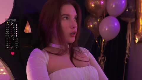 A video of a young woman with fair skin and long, straight brown hair, wearing a white, sheer top with a choker, looking pensive. Background includes a calendar, gold balloons, and dim lighting.