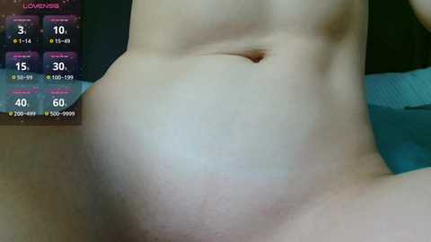 A close-up video of a pregnant woman's bare abdomen, displaying a prominent, round belly and stretch marks. The background includes a digital clock with time and temperature readouts.