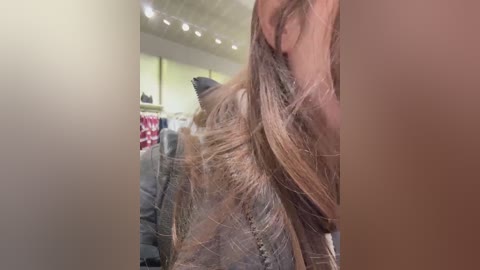 Video of a person with long, blonde hair, partially obscured by a blurred, brown-haired figure in the background, standing in a brightly lit, modern clothing store with shelves and hanging garments visible.