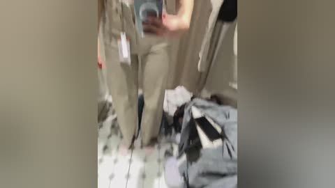 Video of a messy room with beige walls, a cluttered floor, a blue backpack, and clothes hanging.